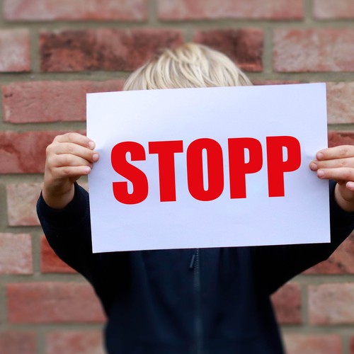 Das Foto zeigt ein Kind, das einen Zettel vor sein Gesicht hält. Das Gesicht ist dadurch verdeckt. Auf dem Zettel steht in großen Buchstaben "Stop!"